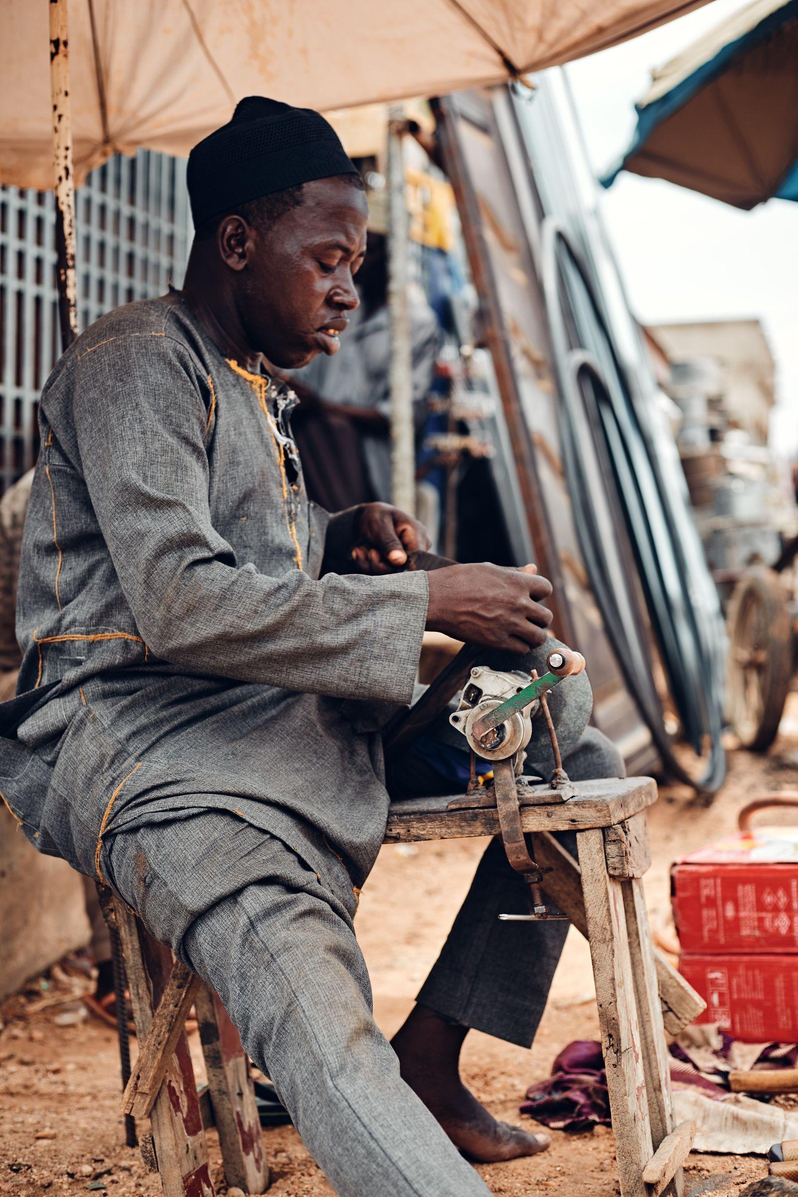 A tailor sewing fabric at an open-air market stall